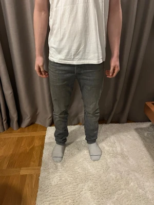 Grå slim jeans från Jack and Jones  - Snygga grå jeans från Jack and Jones med klassisk femficksdesign och svarta läderpatch bak. Jeansen har en slim passform och är tillverkade i mjuk bomullsdenim. Dem är i ett bra skick och passar en person mellan 170-185 cm.