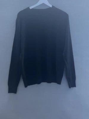 Svart stickad tröja - En enkel svart stickad tröja med rund hals och långa ärmar. Tröjan har en klassisk rak passform och är tillverkad i ett mjukt, stickat material som känns skönt mot huden. Perfekt att matcha med jeans eller kjol för en clean look. Den har inga lappar med strl eller brand men strl är i passform S-M och känns nästan som kashmir.