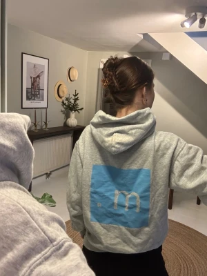 Grå hoodie med blå logga - Grå hoodie med huva. Klassisk känguruficka framtill och mjukt material, perfekt för en chill look. Från en butik på Öland Micke o company. 