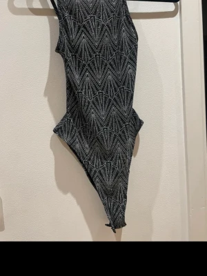 Svartvit baddräkt med grafiskt mönster - Snygg svartvit baddräkt med ett grafiskt, nästan art deco-inspirerat mönster i vitt på svart botten. Klassisk modell med hög benskärning och rund hals. Materialet känns stretchigt och bekvämt, perfekt för stranden eller poolen.