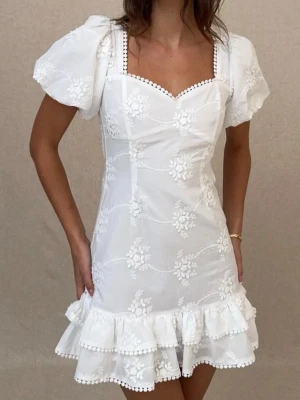 Studentklänning - Superfin vit kort klänning med puffärmar, volangkant och broderade blommor. Klänningen har öppen rygg med gullig rosett. Köpt på nelly för 600kr, endast testad men tyvärr för liten för mig så därav säljer jag💕