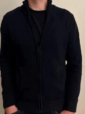 Svart stickad ziptröja med krage - Säljer en svart stickad tröja med dragkedja och hög krage. Tröjan har långa ärmar, ribbade muddar och två fickor framtill. Perfekt för lager-på-lager och enkel att matcha med olika outfits.