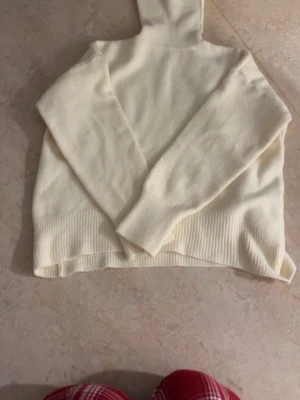 Krämvit polotröja i stickat material - Mysig krämvit stickad polotröja med långa ärmar och bred ribbstickad mudd, säljer denna på grund av att den sitter dåligt på mig den är köpt på  butiken Lovisa Göteborg helt ny aldrig använd.