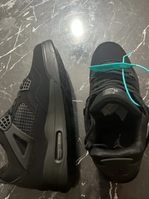 Svarta Air Jordan 4 Retro sneakers - Snygga helsvarta Air Jordan 4 Retro sneakers med klassisk siluett, meshpaneler och detaljer i läder och syntet. Ikonisk Jumpman-logga på hälen och en synlig Air-enhet i sulan. Perfekta för dig som gillar streetwear och sportig stil.