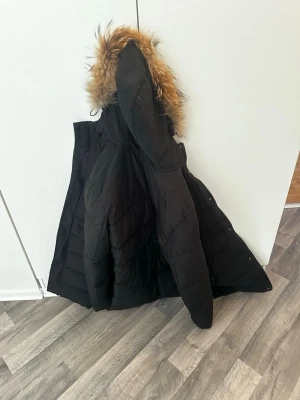 The north face - Svart lång north face jacka med huva och fuskpälsdetalj. Jackan har quiltad design och stängs med dragkedja och knappar. Perfekt för kalla vinterdagar och har en klassisk, stilren look. De står 4XL men de passar för mig so har XL