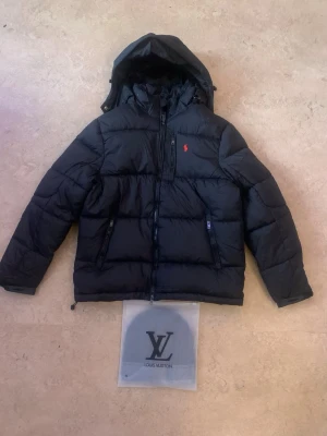 Svart dunjacka från Polo Ralph Lauren - En svart Ralph lauren jacka och en svart märkes mössa som ett bundle