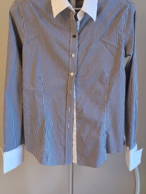 Randig skjorta med vit krage - Klassisk skjorta med smala blå och vita ränder, vit krage och vita manschetter. Skjortan har knappar framtill och lång ärm. Perfekt för en stilren och tidlös look.