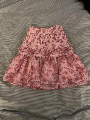 Blommig volangkjol från Gina Tricot - Supersöt kort kjol från Gina Tricot i rosa toner med blommigt mönster och volangdetaljer. Kjolen har smock i midjan för en bekväm passform och är perfekt för vår och sommar. Lätt och luftig känsla!