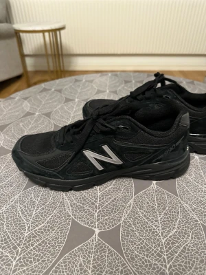Svarta New Balance 990 sneakers - Snygga svarta New Balance 990 sneakers med klassisk siluett. Skorna har mesh och mockadetaljer, samt den ikoniska N-loggan i silver på sidan. Perfekta för dig som gillar stilrena och bekväma sneakers med sportig känsla.