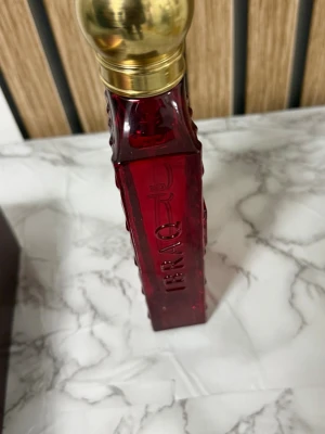 IBRAQ Balas Rose Eau de Parfum - Lyxig parfym från IBRAQ i doften Balas Rose. Flaskan är djup röd med guldfärgat lock och har en elegant, fyrkantig form med detaljerade kanter. Kommer i en matchande röd och guld kartong. Innehåll: 150 ml Eau de Parfum.