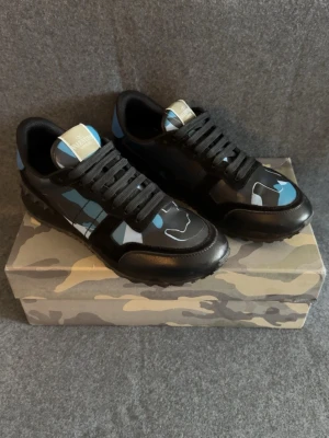 Valentino Rockrunners - Snygga Rockrunners från Valentino i svart med blå camo-detaljer. Skorna har svarta snören, gummisula med rutmönster undertill och Valentino loggan på plösen. Materialmix av läder och mocca som ger en exklusiv känsla och cool look.