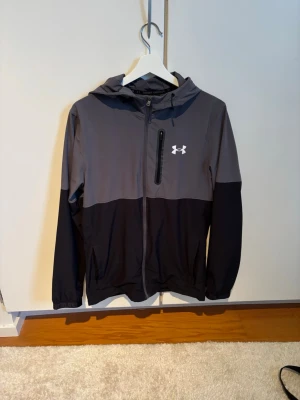 Under armour windbreaker grå - En riktigt snygg och eftertraktad windbreaker i en mörkare grå och en ljus are grå färg, slutsåld över allt och finns inga tecken på användning på denna, som en ny!
