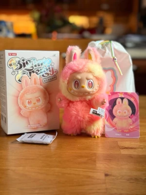 Pop Mart The Monsters Labubu Big into Energy Loyalty  - Söt samlarfigur från Pop Mart, BigMouth Pretty, med fluffig rosa och gul pälsdräkt och kaninöron. Ansiktet är gjort av plast med stora färgglada ögon och ett brett leende. Kommer med originalförpackning, tygpåse och samlarkort.