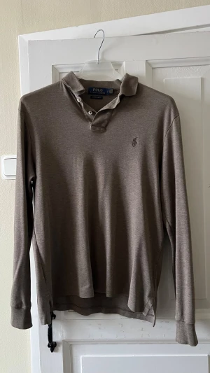 Brun henley från Polo Ralph Lauren - Snygg brun henley från Polo Ralph Lauren med lång ärm och klassisk krage. Skjortan har knappar vid halsen och diskret logga broderad på bröstet. Tillverkad i mjukt bomullsmaterial som känns skönt mot huden.
