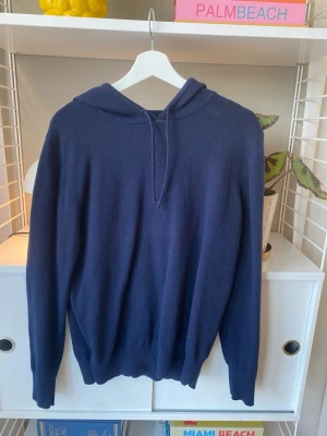 Mörkblå stickad hoodie - Mysig mörkblå stickad hoodie med dragsko i huvan. Tröjan har en avslappnad passform och långa ärmar. Perfekt för lager-på-lager och chill dagar. Materialet känns mjukt och skönt mot huden.