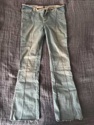 Ljusblå bootcut jeans med rå kant - Super snygga och trendiga bootcut jeans med låg midja. Kanten är fransig och gör jeansen extra snygga och unika. De är i väldigt bra skick och sitter jätte skönt då materialet inte är för stretchigt och inte heller för hårt. Fråga gärna om mått!
