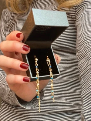 Guldiga örhängen med blåa och vita pärlor - Säljer ett par jättefina guldiga örhängen med hängande kedjor och små blå och vita pärlor. Upptill har de också en liten kristall. Örhängena består av flera länkar och pärlor som ger en cool och trendig look. Är osäker på material (därav priset) och misstänker att de inte är sterlingsilver beklädda med guld, utan snarare mässing eller nåt i den stilen. Har dock aldrig fått problem med dem eller utslag.