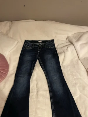 Mörkblå bootcut jeans med broderad ficka - Snygga mörkblå jeans från Gina tricot med bootcut passform. Jeansen har kontrastsömmar och en bakficka med broderade fjädrar och paljettdetaljer. Klassisk femficksmodell och coola detaljer som ger extra edge till outfiten.