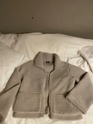 Beige teddyjacka med dragkedja - Supermjuk och mysig beige teddyjacka från 157. Jackan har en rak passform, hög krage och dragkedja framtill. Perfekt för kyliga dagar och enkel att matcha med allt. Två stora fickor framtill och långärmad modell.