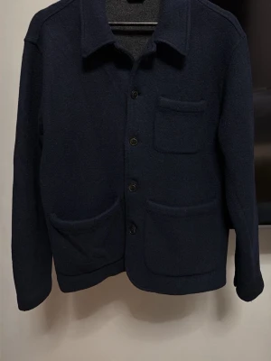 Mörkblå overshirt från Polo Ralph Lauren - Säljer en mörkblå overshirt från Polo Ralph Lauren i ull. Jackan har tre stora fickor framtill, knäppning med svarta knappar och klassisk krage. Perfekt för lager-på-lager och riktigt snygg till jeans eller chinos. Den har tyvärr råkat hamna med i tvätten så den har blivit en small. Men den är fortfarande i ett väldigt bra skick nästa intill perfekt. Ny pris 4295 kr