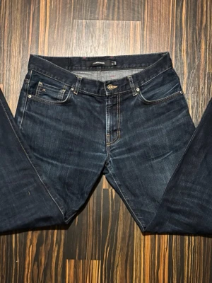 Mörkblå jeans från J.Lindeberg  - Säljer ett par mörkblå jeans från J.Lindeberg i klassisk femficksmodell. Jeansen har kontrastsömmar, normal passform och raka ben. Tillverkade i slitstarkt denim med snygg tvätt och diskret JL-detalj på myntfickan. Perfekta till vardagslooken. Jeansen är nya nu pris på dessa är 1600kr