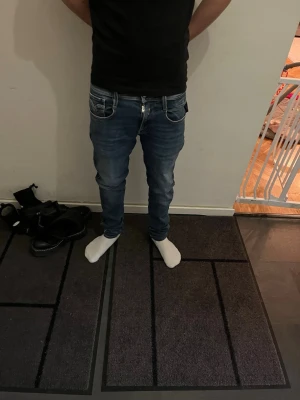 Replay Anbass blå jeans slim fit - Säljer ett par Replay Anbass jeans i snygg blå tvätt med slim fit och klassiska fem fickor. Jeansen har låg midja, dragkedja och Replay-logga på fickan. Materialet är mjukt jeans-tyg med snygga slitningar och kontrastsömmar. Perfekt för dig som gillar stilrena och moderna jeans. Storleken är 29/32. Modellen är 168 cm lång och väger 55 kg. Det är bara att höra av sig vid frågor eller funderingar 😀