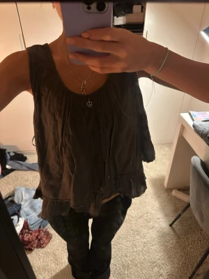 mörkgrå linnetopp med volangkant - snygg och luftig ärmlös topp i grå nyans. mjukt, lätt material med fint fall och rynkad detalj framtill. dekorariv liten berlock (ihåligt hjärta) ger en extra detalj. perfekt till vardag men även lätt att klä upp. sommarkvällar är en dröm i detta linne😍