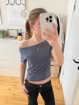 Mörkblå croppad topp med offshoulder - En blågrå smått croppad topp i mjuk bomull. Toppen har korta ärmar och en snygg skärning som gör att man kan bära den på flera vis så som en båtkrage eller off the shoulder på en sida. Den är storlek L men är liten i storleken då den passar mig som brukar ha XS. Tryck gärna på köp nu!❤️