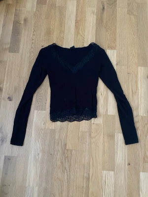 Svart spetsdetaljerad topp Gina Tricot - Säljer en svart långärmad topp från Gina Tricot i storlek XS. Toppen har v-ringning och fina spetsdetaljer både vid halsen och längst ner. Materialet är mjukt och stretchigt, vilket gör den bekväm att bära. Perfekt för dig som gillar en enkel men ändå snygg look.