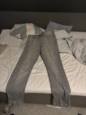 Grå jeans från Jack & Jones - Säljer ett par grå jeans från Jack & Jones med klassisk femficksdesign och raka ben. Jeansen har en snygg tvättad look och är tillverkade i slitstarkt bomullsmaterial. Passar perfekt till en avslappnad stil och funkar året runt.
