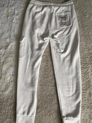 Vita mjukisbyxor från Hoodrich M - Säljer mina vita Hoodrich byxor strl M (nästan nya). De är äkta och bara använda 1–2 gånger, annars har de mest legat i garderoben. Skickar gärna fler bilder eller mått om du vill. Materialet är 80% bomull och 20% polyester för en mjuk och bekväm känsla.