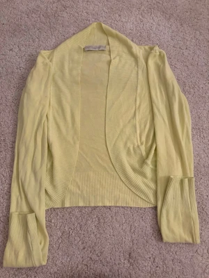 Ljusgul kofta från Cristina Gavioli - Snygg ljusgul kofta från Cristina Gavioli med öppen front och ribbade muddar samt nederkant. Långärmad modell i mjukt, tunt material som passar perfekt till lager på lager. Enkel och stilren design som är lätt att matcha.