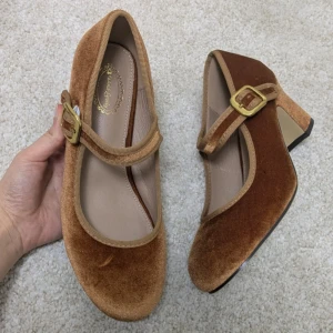 Bruna Mary Jane pumps i sammet - Oanvända, bekväma med dämpad sula 🍭                Säljer ett par bruna Mary Jane pumps från Classic Royalty med rund tå och låg klack. Skorna är gjorda i mjuk sammet och har ett justerbart band med guldfärgat spänne över foten. Perfekt för dig som gillar vintagevibbar och snygga detaljer.