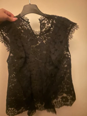 Svart spetsblus från Zara XS - Säljer en svart blus från Zara i storlek XS. Blusen är ärmlös och helt täckt av vacker spets med blommönster och fina kanter. Perfekt för dig som gillar detaljer och vill ha en elegant look. Tillverkad i polyester.