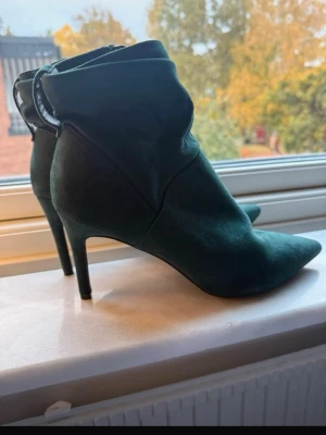 Gröna mocka stövletter med spetsig tå - Säljer ett par mörkgröna stövletter i mjuk mocka med smal hög klack och spetsig tå. Skorna har dragkedja på insidan och en elegant, stilren look som passar perfekt till höstens outfits.