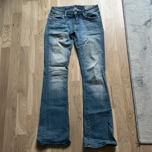 Crocker Pep! Boot blå bootcut jeans 27/32 - Snygga blå bootcut jeans från Crocker, modell Pep! Boot i storlek 27/32. Midjemåttet är 34cm och innerbenslängden är 81cm. Klassisk femficksdesign med slitningar och ljus tvätt på låren och bak. Jeansen har normal passform och är tillverkade i mjukt denim med bruna sömmar och läderpatch bak. Den ser inte jättefina ut på bild men om man är intresserad av att köpa dem så kan jag skicka bättre bilder.