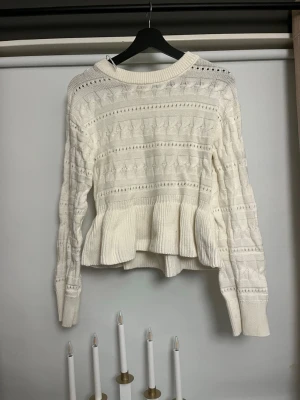 Vit stickad volangtröja Gina Tricot - Supersöt vit stickad tröja från Gina Tricot med volangdetalj nedtill. Tröjan har ett fint strukturmönster, rund halsringning och långa ärmar. Perfekt för dig som vill ha en mysig och trendig look till hösten eller vintern.