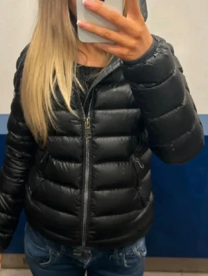 Svart pufferjacka med huva - Säljer en svart pufferjacka från Colmar med huva och två dragkedjeförsedda fickor. Jackan har quiltad design, lång ärm och en klassisk passform. Perfekt för kyliga dagar och enkel att matcha till olika outfits. Storlek 40 italiensk storlek motsvarar XS i svensk storlek