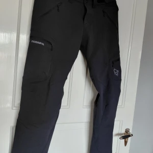 Svarta Svalbard Flex1 byxor från Norrøna - Svarta Svalbard Flex1 byxor från Norrøna med flera dragkedjeförsedda fickor och broderad logga på benet. Byxorna är tillverkade i ett slitstarkt syntetmaterial och har en sportig, funktionell look med smal passform. Perfekta för utomhusaktiviteter.Stl: M Mitt Pris, : 50:-