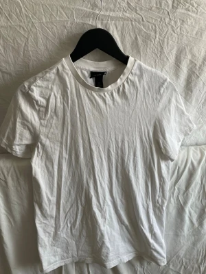 Vit basic t-shirt från H&M - En klassisk vit t-shirt från H&M med rund hals och korta ärmar. Tillverkad i mjuk bomull som känns skön mot huden. Perfekt att styla med jeans eller under en skjorta för en clean look. (Du får med två stycken)