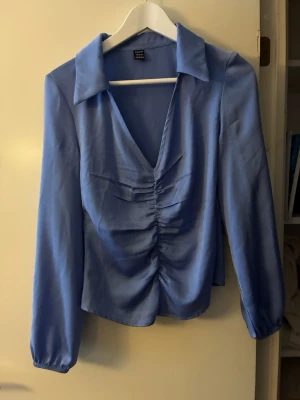 Snygg blus med rynk fram  - Snygg blus med rynk fram. Satinliknande material.  Dragkedja på sidan. 