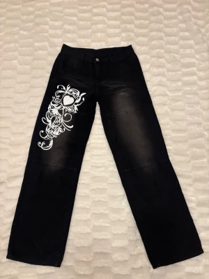 Svarta Jeans Med Tryck - Supersnygga svarta jeans i storlek 34/36 med ett coolt vitt tryck på ena benet. Rak passform med lite vidare ben och sitter jättefint. Köpta från någon hemsida men minns tyvärr inte exakt vilken. Använda  en gång💕