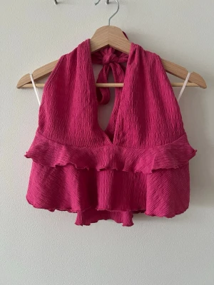 Rosa volang topp från SHEIN - Säljer en rosa linnetopp från SHEIN i storlek M. Toppen har volangdetaljer, knyt i nacken och är ärmlös. Materialet är lätt och strukturerat, perfekt för varma dagar. Supersnygg till både jeans och kjol!
