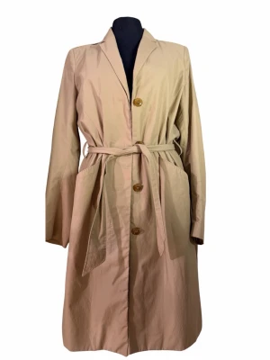 Beige trenchcoat, Filippa K - Stilren beige trenchcoat från Filippa K med klassisk krage, knytskärp i midjan och stora fickor. Jackan har knappar framtill och är tillverkad i ett lätt bomullsmaterial. Perfekt för dig som gillar minimalistisk och clean look. Finns några imperfections (se bild)