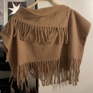 Beige poncho med fransar - Säljer en beige poncho med långa fransar längs kanterna. Mjuk och skön, passar till både höst och vår. Aldrig använd!!