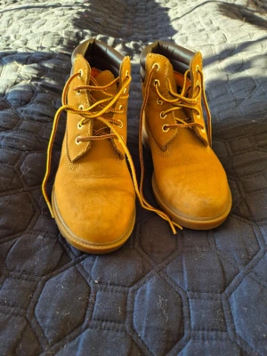 Bruna Timberland boots i mocka - Säljer ett par klassiska Timberland boots i ljusbrun mocka med gul- och brunmönstrade snören. Skorna har rund tå, vadderad kant och robust sula. Insidan är fodrad med orange textil och Ortholite-innersula för extra komfort. Används 2 ggr