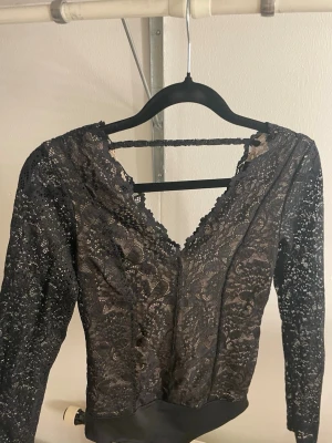 Svart spetsblus med v-ringning - Säljer en svart blus med lång ärm i spetsmaterial och v-ringad.