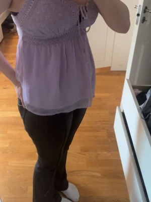 Ljuslila broderad linnetopp - Säljer en söt ljuslila linnetopp med broderade detaljer och knyt framtill. Toppen har tunna axelband och ett luftigt, flowy tyg som ger en romantisk vibe. Perfekt till sommaren och enkel att styla med jeans eller kjol.