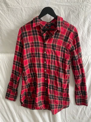 Rutig röd skjorta från Gant - Klassisk rutig skjorta från Gant i rött, svart och vitt. Skjortan har lång ärm, knappar framtill och en bröstficka. Tillverkad i mjuk bomull och har en avslappnad passform. Perfekt för dig som gillar en tidlös och chill stil.