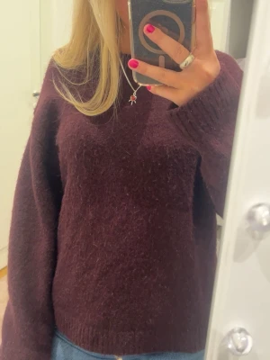 Vinröd stickad tröja - Säljer en mysig vinröd stickad tröja med långärmad passform och ribbade muddar vid ärmslut och nederkant. Perfekt för kyliga dagar och enkel att matcha med jeans eller kjol. Tröjan har en loose fit och är superbekväm.